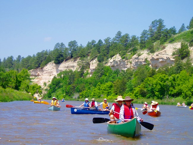 Canoes on a river with tan bluff and blue sky behind.