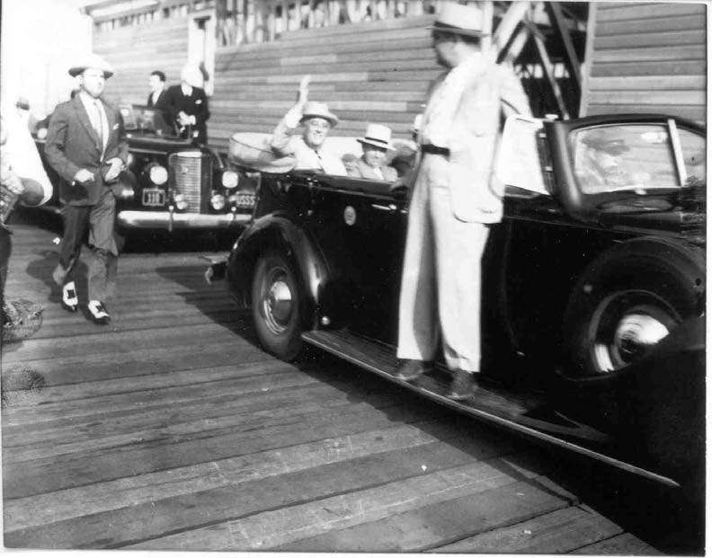 President Franklin D Roosevelt sits in the back of a black car, waving