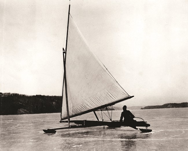 A shadowy figure sailing an ice boat on a frozen river.