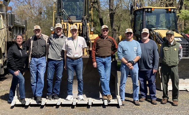 Eight smiling people standing shoulder-to-shoulder with bulldozer machines behind them
