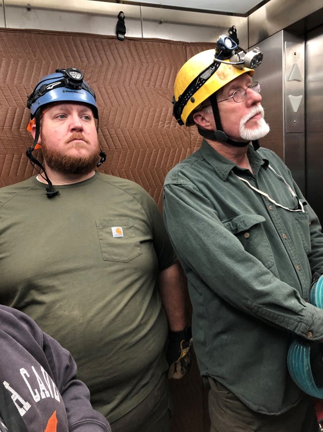 two people with climbing helmets and headlamps standing in an elevator
