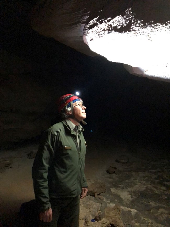 a person wearing a climbing helmet examines a cave wall