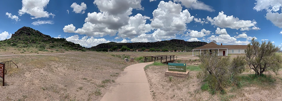Fort Davis National Historic Site A landscape view of Fort Davis buildings, grassland, and rocky hills under fluffy clouds.