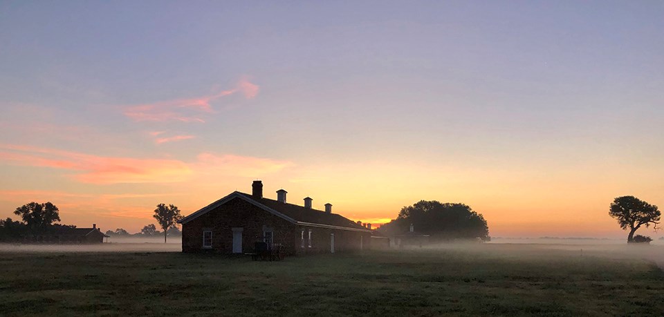 A one-floor, sandstone building with multiple chimneys stands out amidst the morning fog.