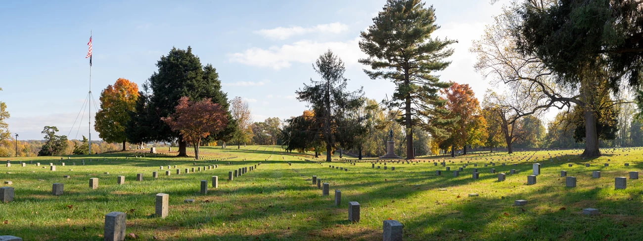 Fredericksburg National Cemetery in fall Wide view of national cemetery landscape in fall with flagpole, rows of similar headstones, and scattered trees and monuments