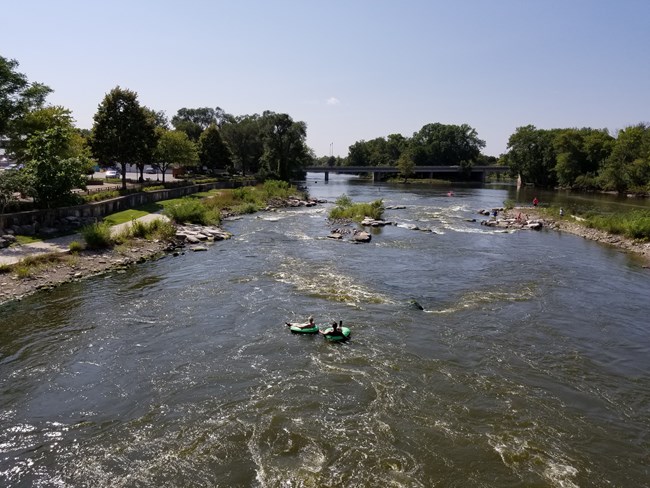 Two people in inner tubes float gently down a wide river.