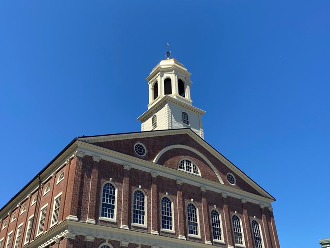 Top of a brick building and its cupola in front of a bright blue sky.