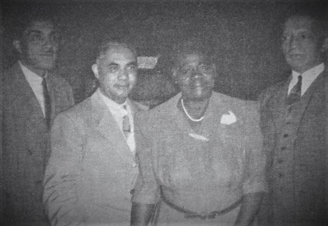 Three men and a woman stand together all wearing business clothes.