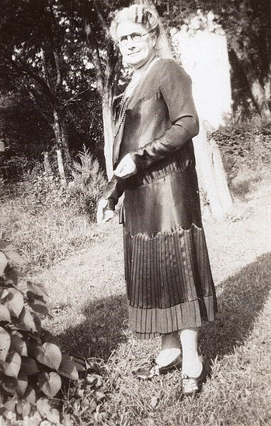 A woman with glasses stands in a garden