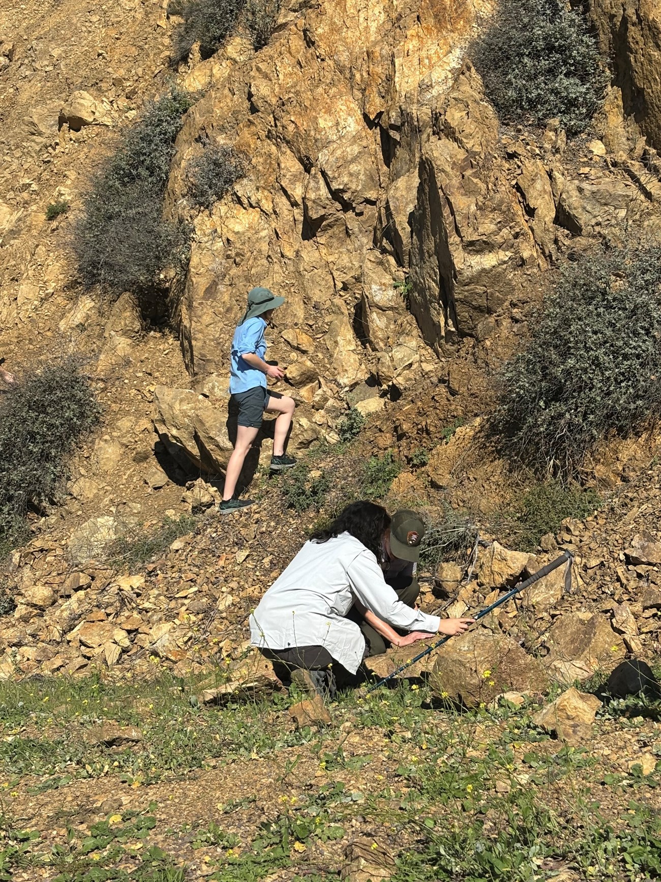 Three people investigate features on and next to a steep rocky slope.
