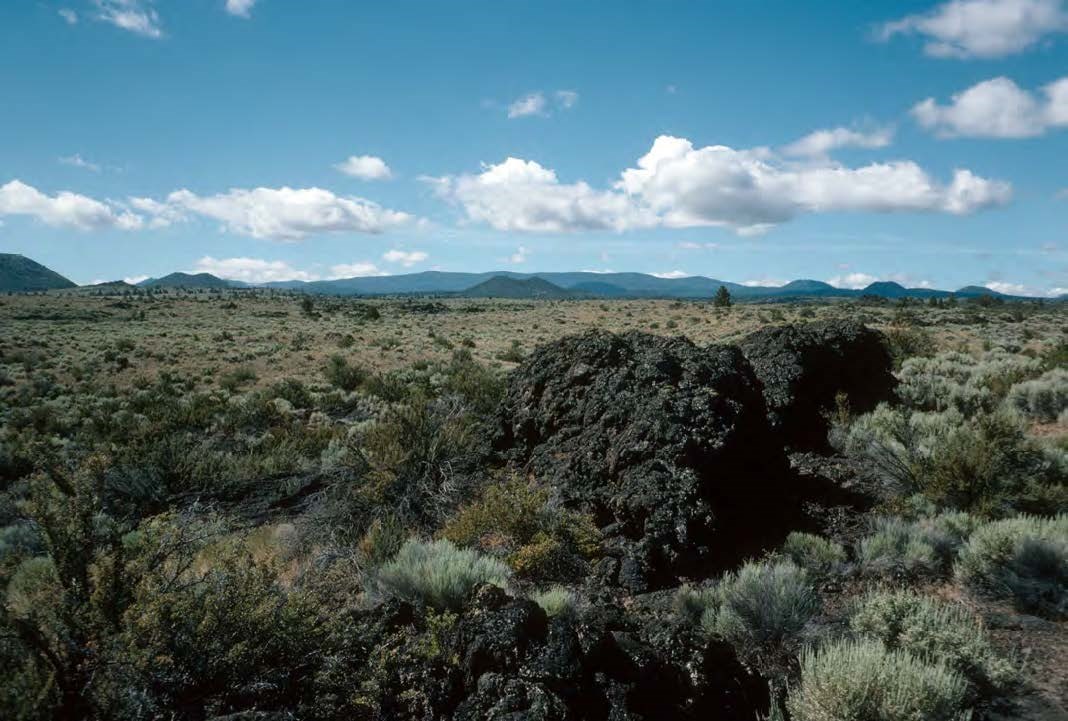 photo of a volcanic landscape with blocky rocks in the foreground and low mountains in the distance.