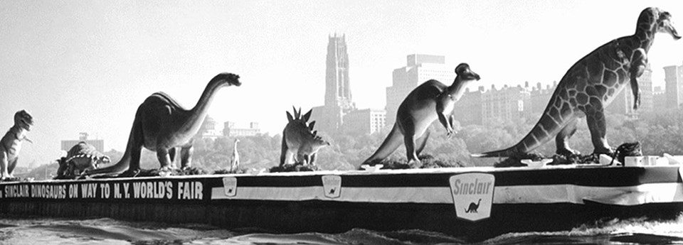 6 dinosaur statues in a line on a badge Ney York City skyline in background.