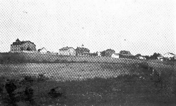 Black and white landscape of small buildings on a hill with a brick school building at front