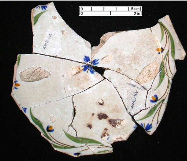 pearlware saucer pieces of a hand painted pearlware saucer with blue, green, and yellow hand painted floral design, arranged so the pieces fit back together.