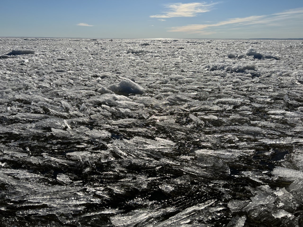 An image of sea ice shining in the sun in various melt stages that look like layers of flakes amidst chunks on the ocean’s surface