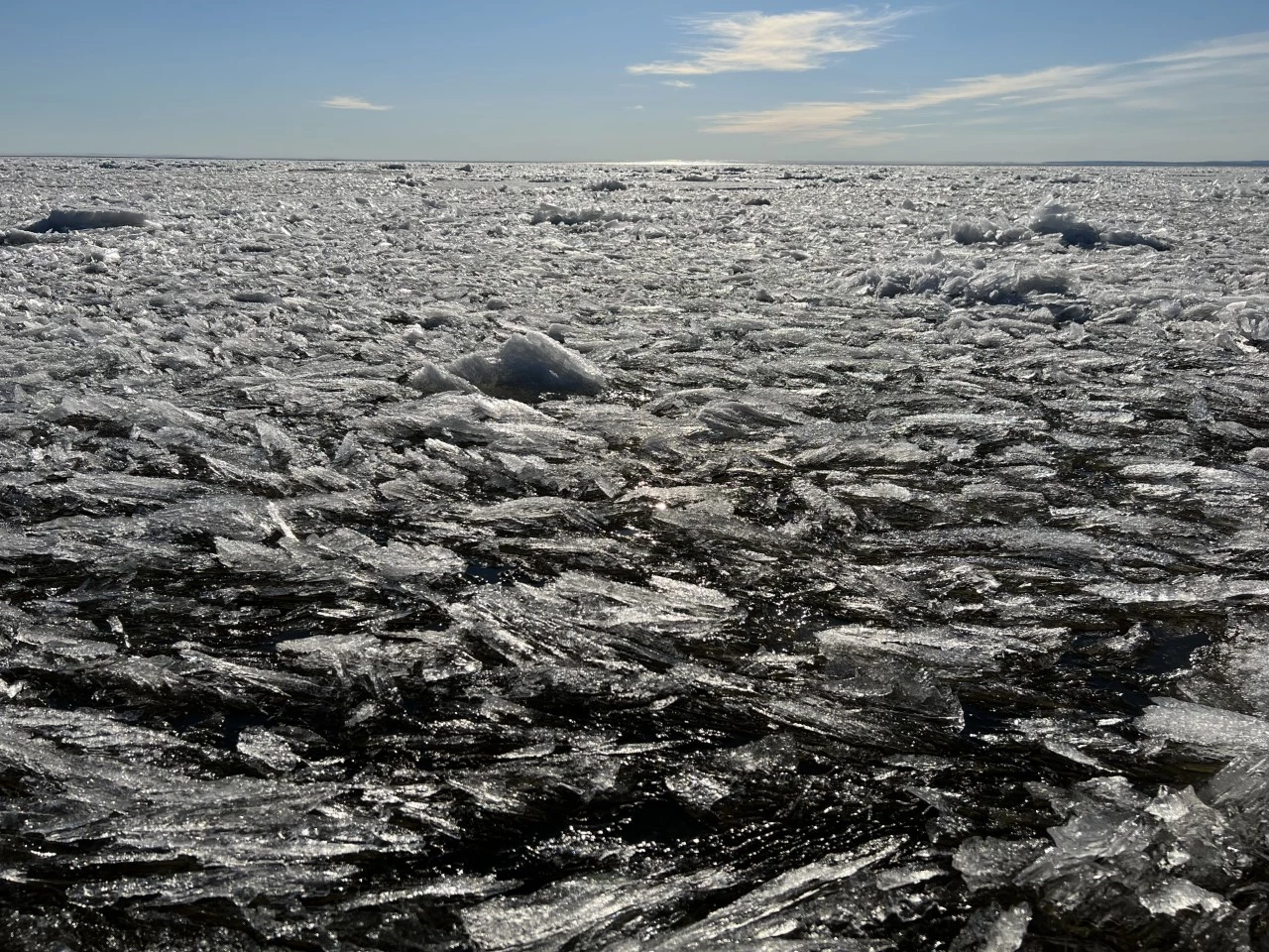 An image of sea ice shining in the sun in various melt stages that look like layers of flakes amidst chunks on the ocean’s surface