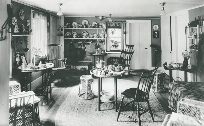 A tea set sits a on small round table with chair in the center of a room; curios and tables line the walls.