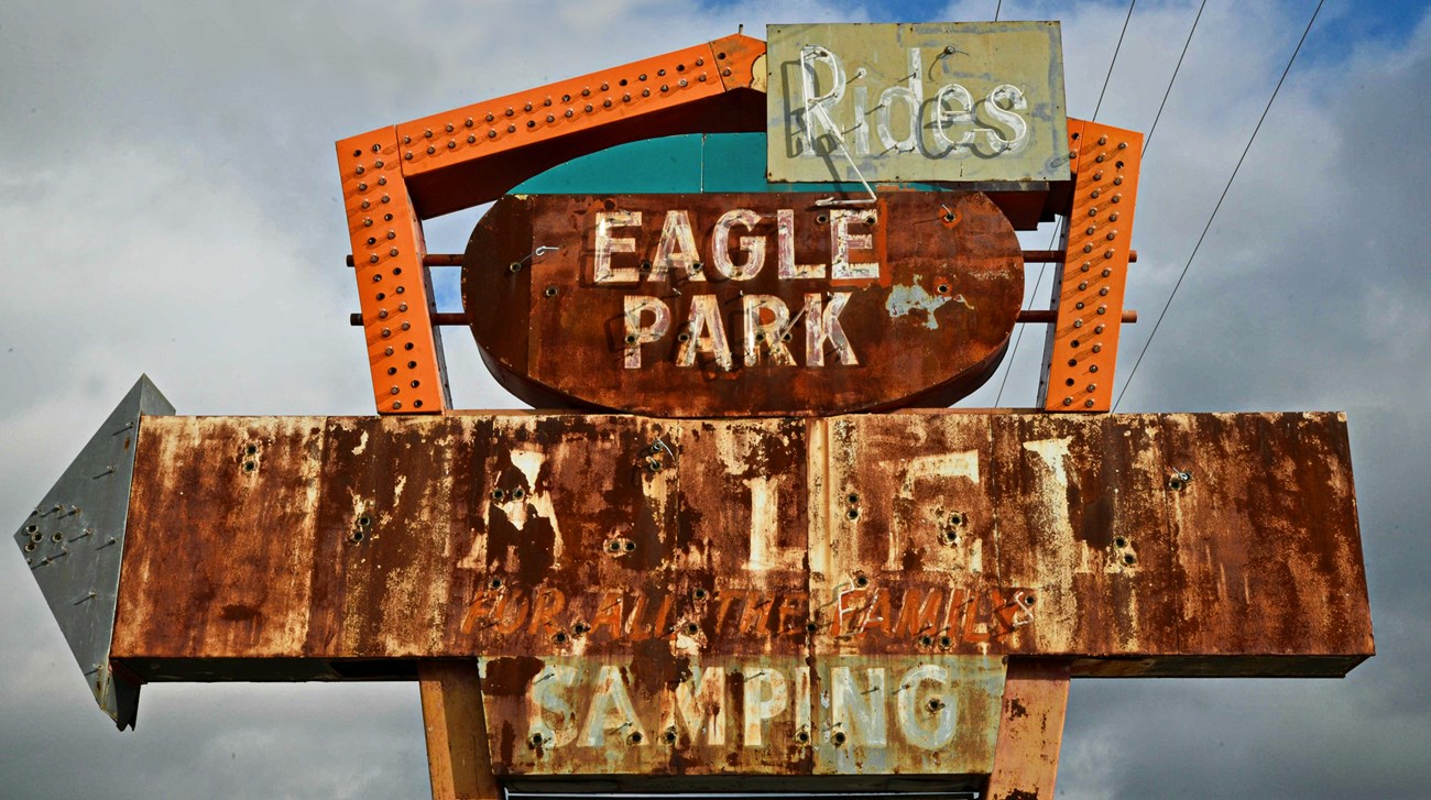 Eagle Park Rusting sign with arrow missing light bulbs with text reading rides, Eagle Park, and other lettering not legible.