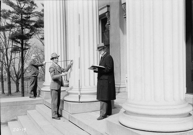 Three men measure a column.