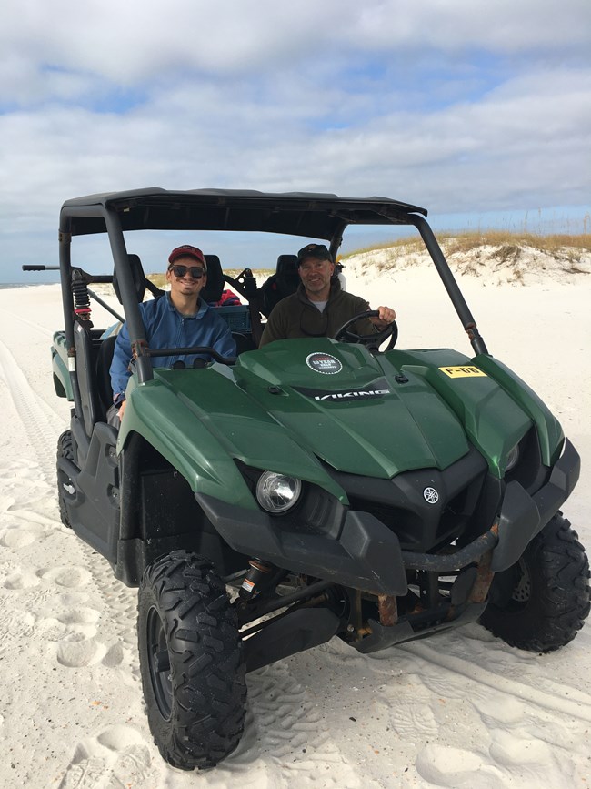 photo of two people sitting in an off road vehicle on a beach