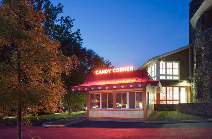 Brightly lit words Candy Corner on the red roof of small building with a wall of windows in the front.