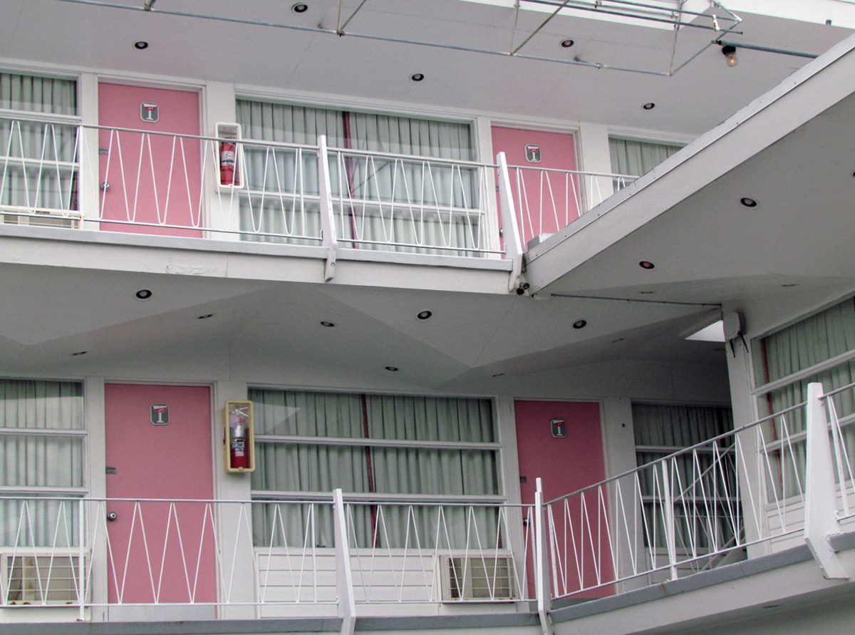Two pink doors on two floors: entry to motel room from white outdoor balconies.