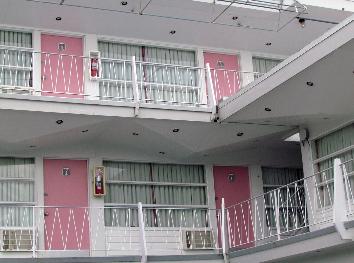 Pink Champagne Hotel Two pink doors on two floors: entry to motel room from white outdoor balconies.