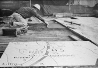Man wearing a hardhat kneeling on the spreading mortar with a trowel; section map in foreground.