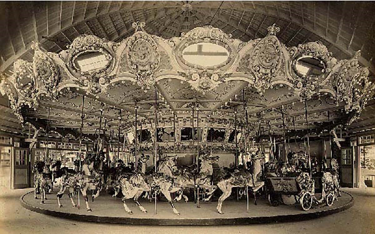 Historic photo of a carousel with three rows of horses mounted on poles with an ornate trim around the top.