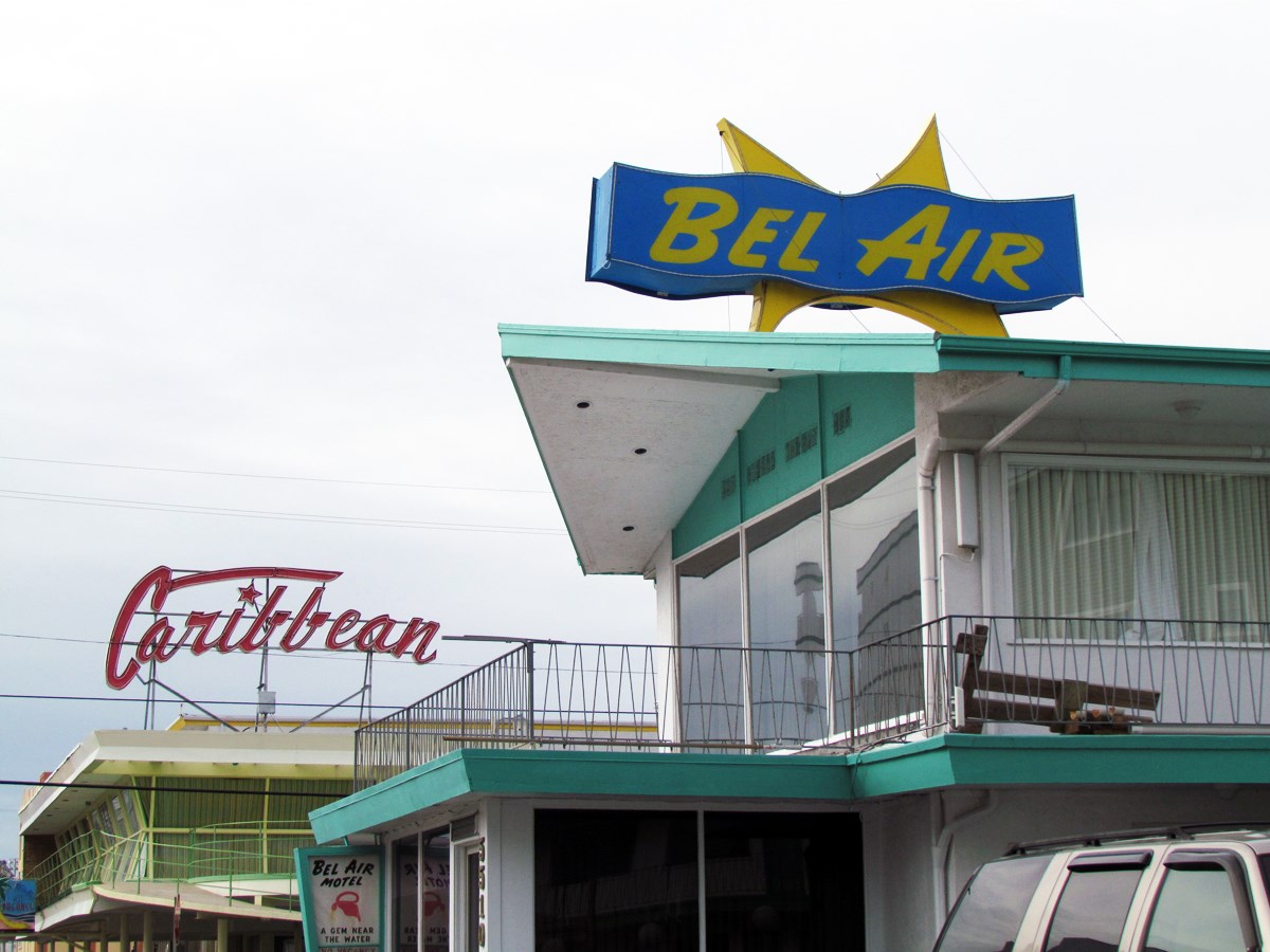 Two motel signs on buildings with bright colored trim Bel Air in front and Caribbean in back.