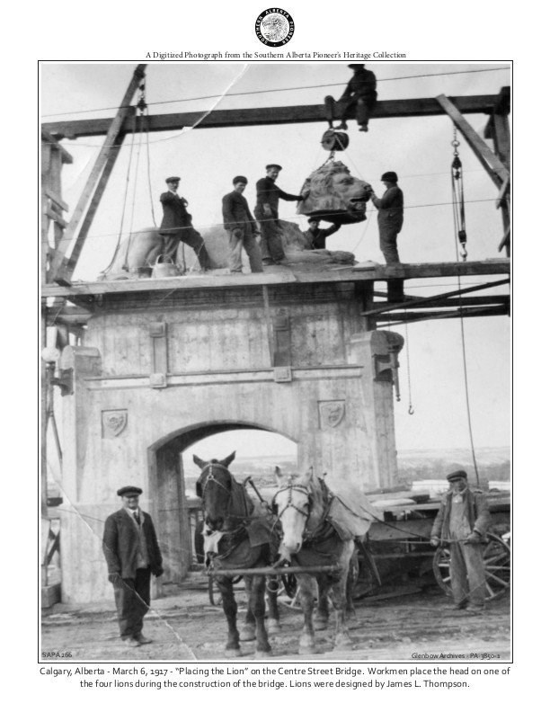 Men on scaffolding placing a lion head on a top a tall archway platform.