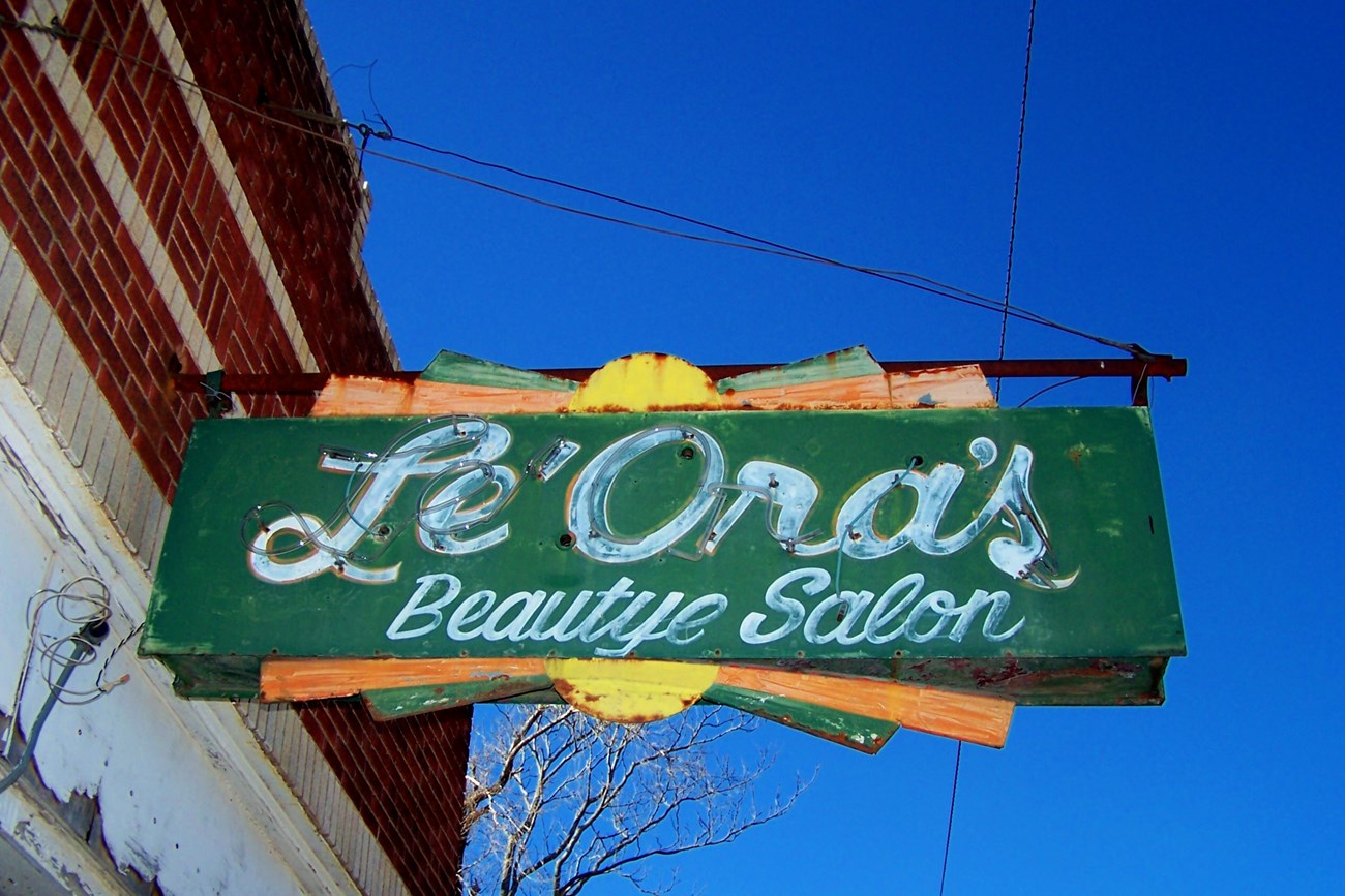 Weathered neon green rectangular sign with white script text reading Le'Ora's Beautye Salon.