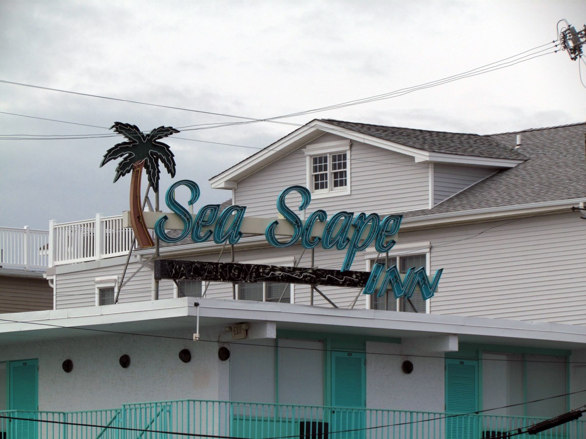 Turquoise sign with a palm tree on top of white building text reads Sea Scape Inn.