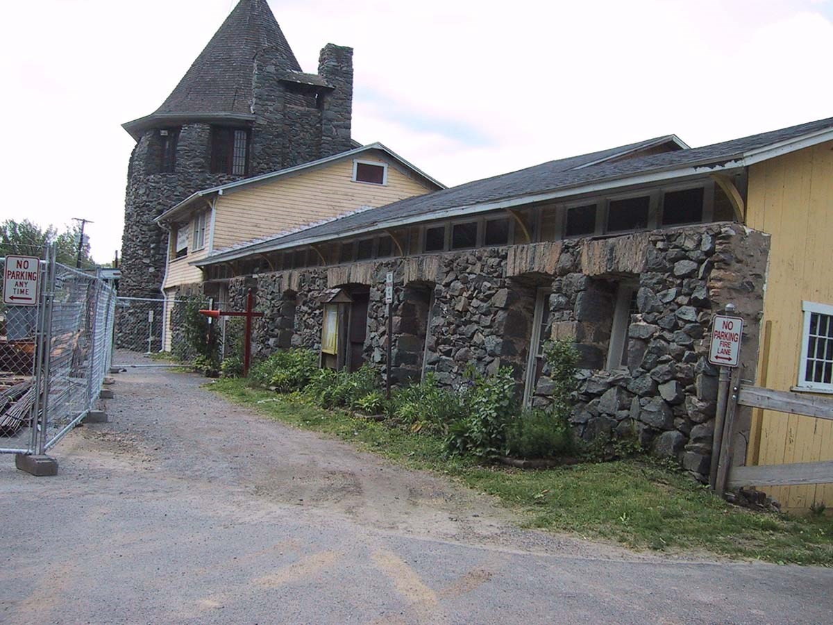 Gravel drive in front of Stone façade long narrow building in line with yellow barn and three-story stone turret.