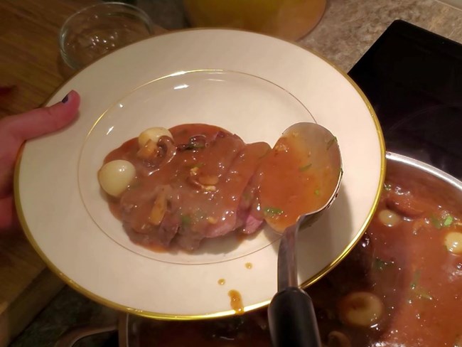 lt= Plate of beef with sauce being served from a stove on a pan