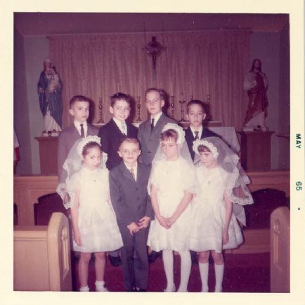 8 children stand in two orderly rows wearing communion attire