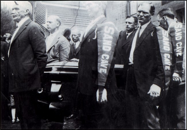A black and white photo of a group of men carrying a coffin.