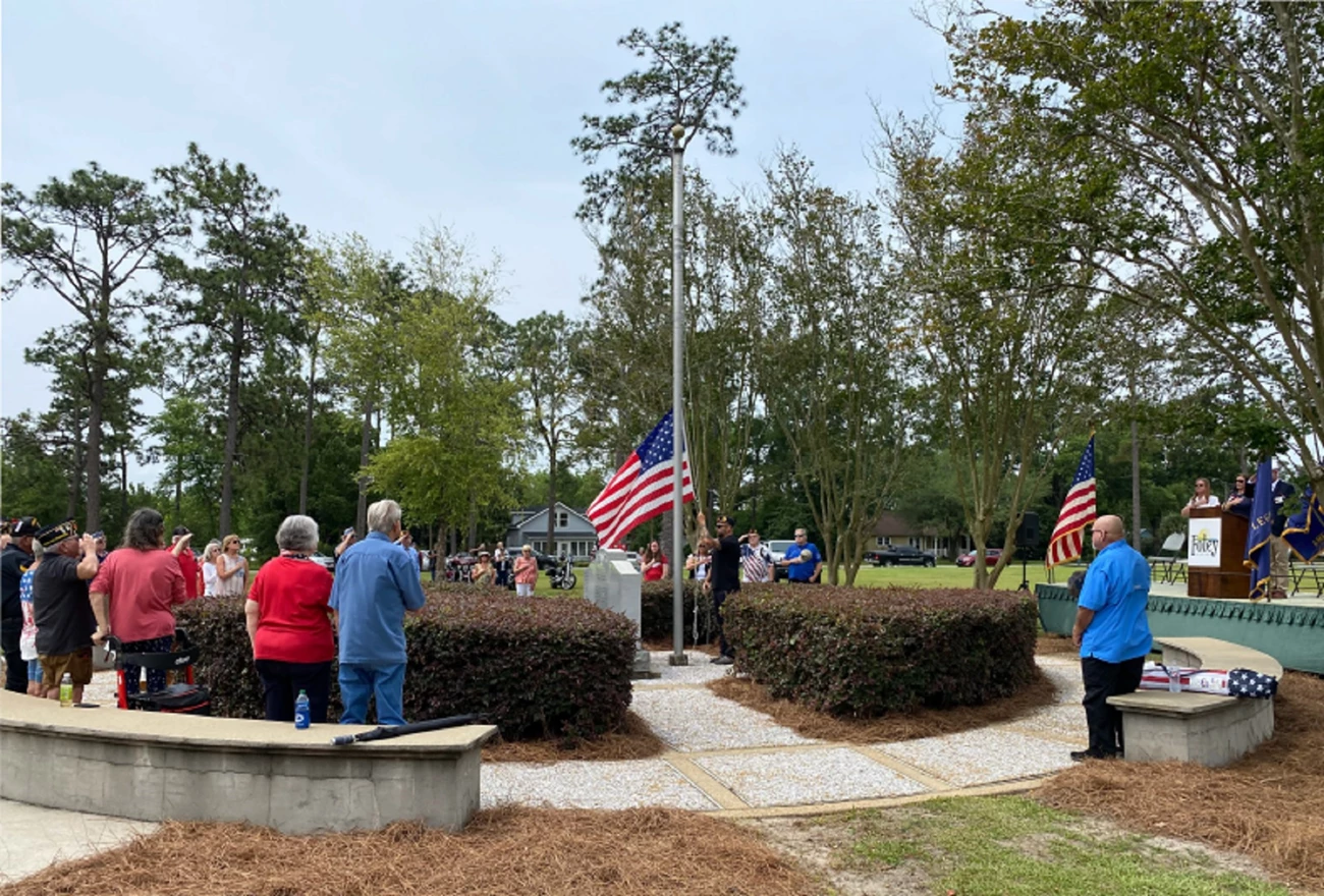 Foley, Alabama Veterans Memorial people gathered around a flagpole and stone markers watching flag being raised