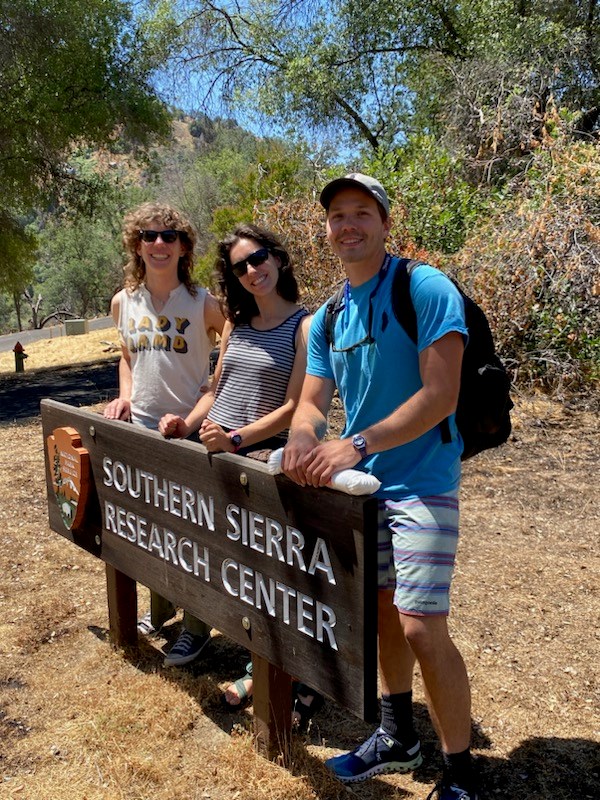 Three people stand behind a National Park Service sign that says Southern Sierra Nevada Research Center and smile toward the camera.