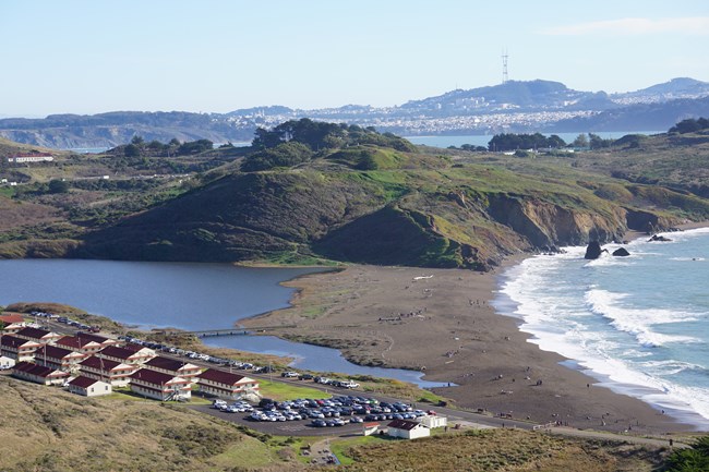 Looking down at rows of red-roofed buildings, a lagoon, and a beach from a trail high above.