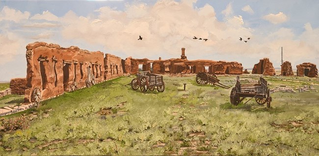 Adobe ruins stand in a grassy field accented by wagons