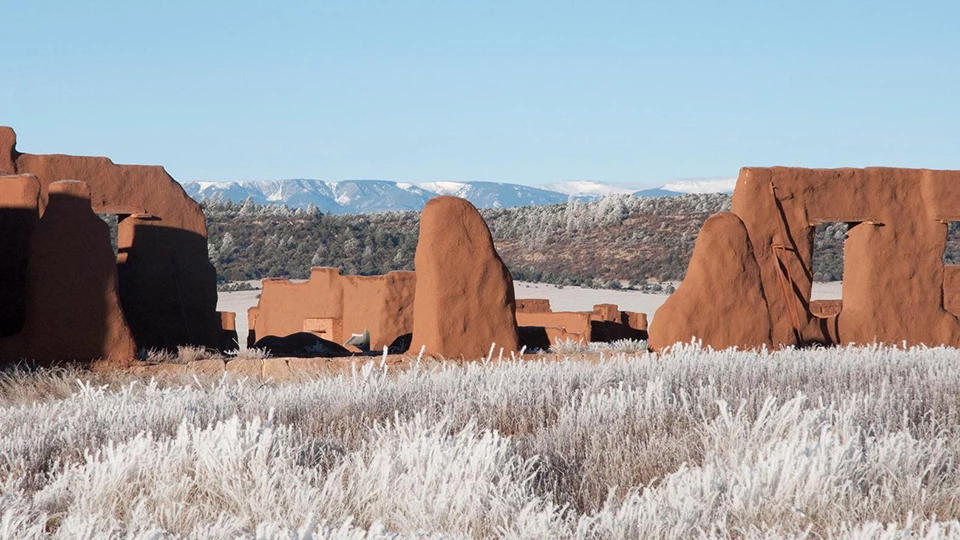 Fort Union National Monument Brown mud ruin walls in a valley of snow covered grasses with snow covered mountains behind them.