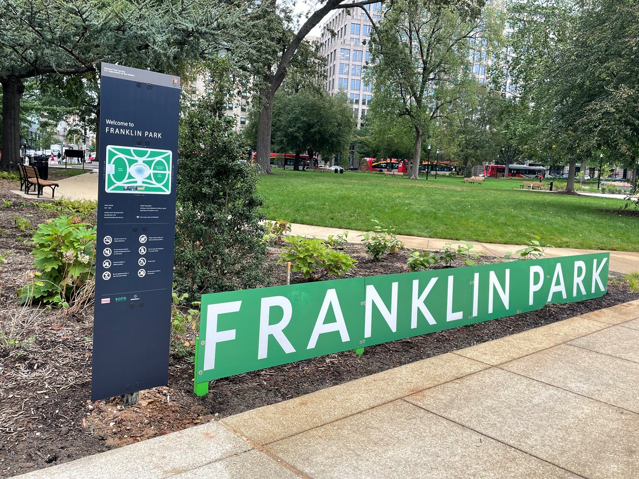 Franklin Park Sign with green grass and trees and busses in the background.