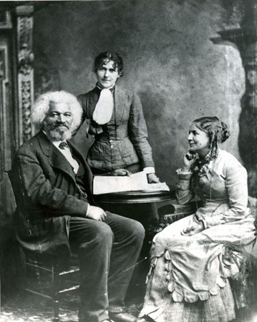 From left to right, photograph of Frederick Douglass, Eva Pitts, Helen Pitts sitting for a portrait. Both Frederick and Eva looking into the camera while Helen looks at Frederick.