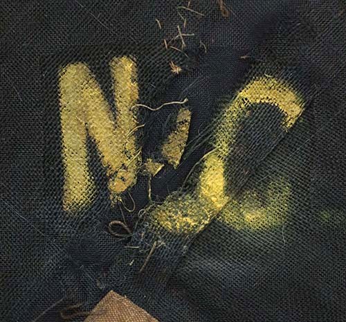 N.C. seen on 2nd N.C. flag A close-up photo of the letters "NC" panted in yellow over black fabric.
