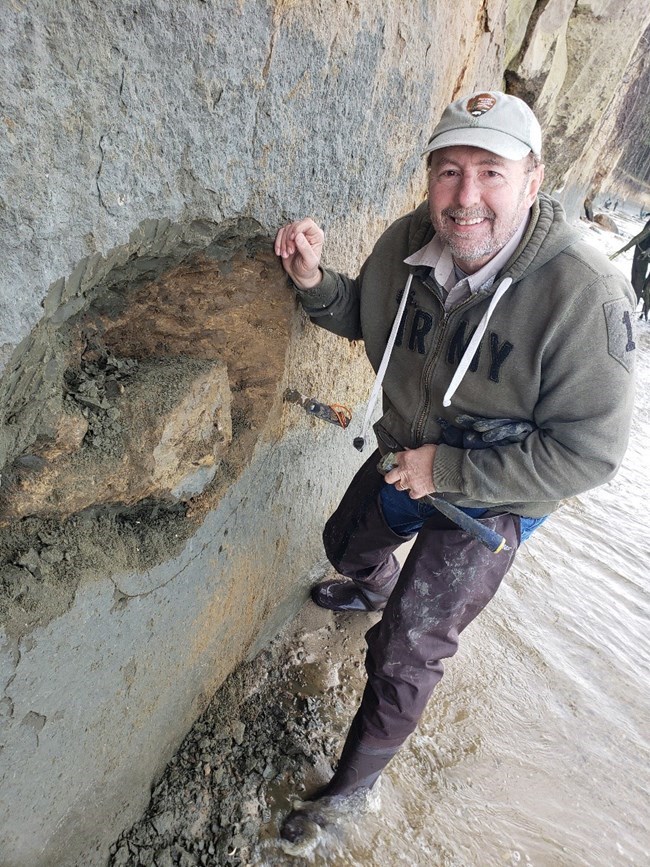 GEWA Vince Santucci with Fossil 2 Paleontologist next to a fossilized dolphin skull in a rock face
