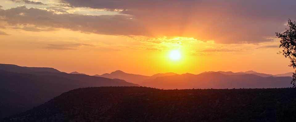A brilliant orange, pink, and yellow sunset over purple and pink mountains.