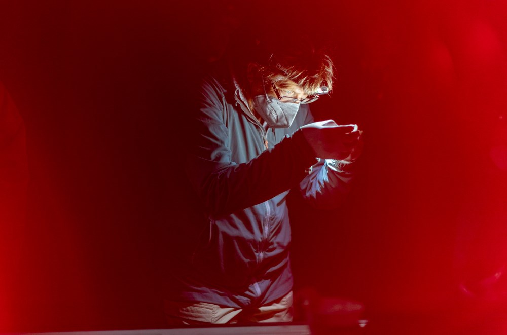 A person wearing a headlamp holds something between their hands. There's a red haze over the image.