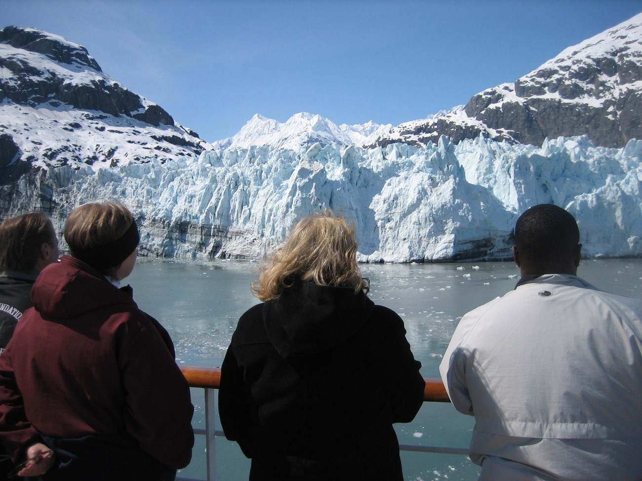 Glacier Bay four people stand on boat deck and look out at glacier