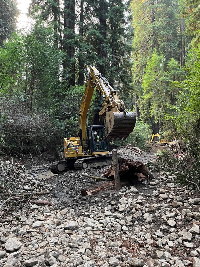 An excavator in creek bed moving small logs